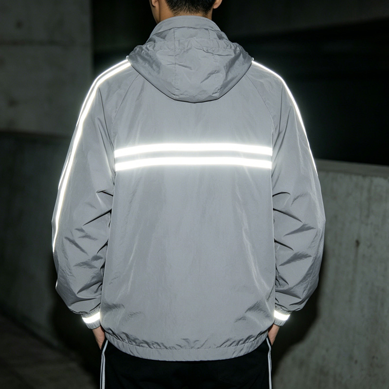 পুরুষদের ধূসর রঙের প্রতিফলক উইন্ডব্রেকারের পিছনের দৃশ্য, যেখানে পিঠে দুটি অনুভূমিক প্রতিফলক স্ট্রাইপ দেখা যাচ্ছে।