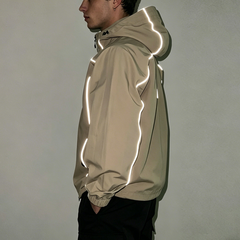 Kilid nga talan-awon sa beige reflective windbreaker sa mga lalaki, nga nagpakita sa mga detalye sa reflective piping sa mga abaga, manggas, ug hood