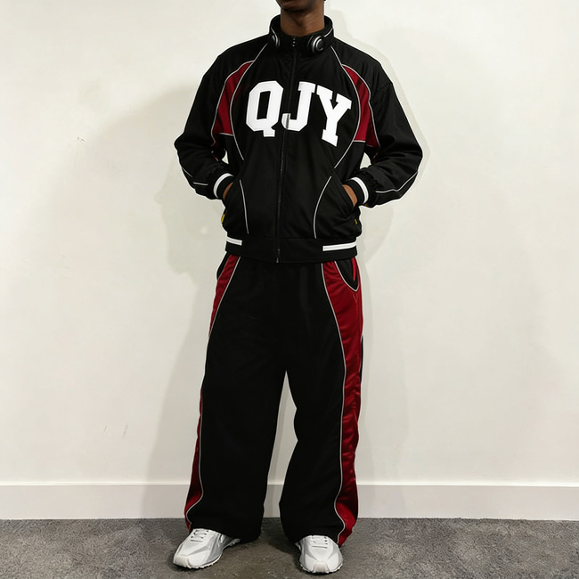 Imbere hagaragara umugabo wambaye tracksuit ifite zipu, amaboko ye ashyizwe mu mifuka y'ikoti