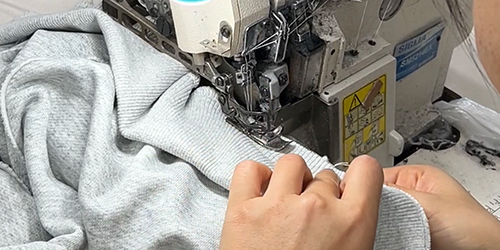 Factory worker stitching garments during bulk apparel manufacturing process.