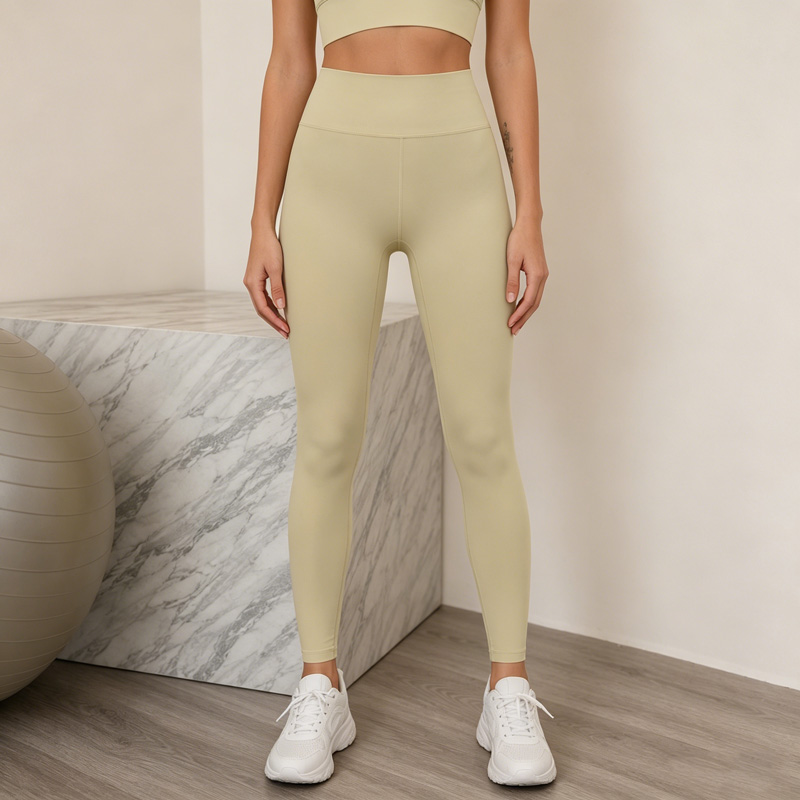 Woman standing with both feet apart and arms relaxed, wearing beige high waisted leggings with white sneakers.