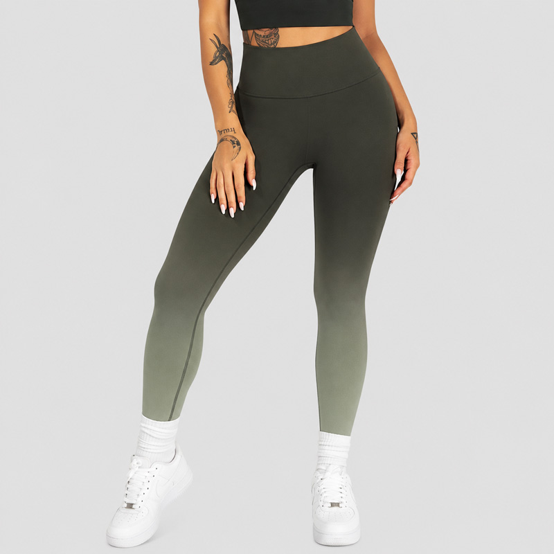 Woman standing with one leg slightly forward, wearing olive green ombre leggings paired with white sneakers.