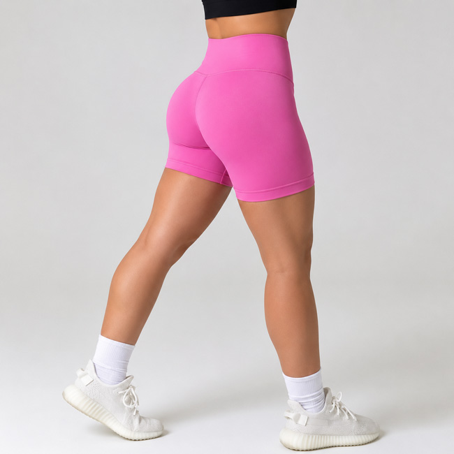 Side angle view of a woman stepping one foot back while wearing hot pink fitted workout shorts.