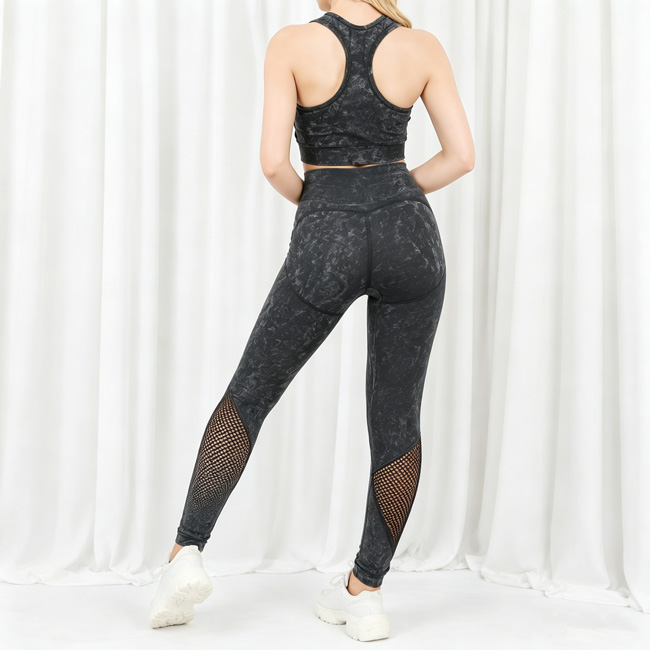 Back view of a woman standing with one leg slightly bent, wearing a black washed yoga set with mesh panel detailing.