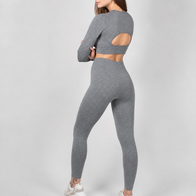 Back angle view of a woman standing with her arms crossed, wearing a gray long sleeve workout set with a back cutout detail.