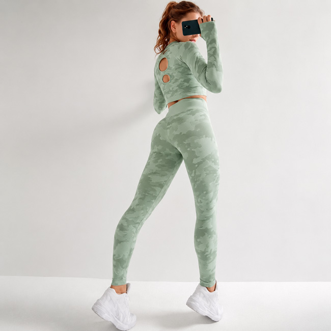 Back view of a woman turning slightly while wearing a sage green marble print workout set with back cutout details.