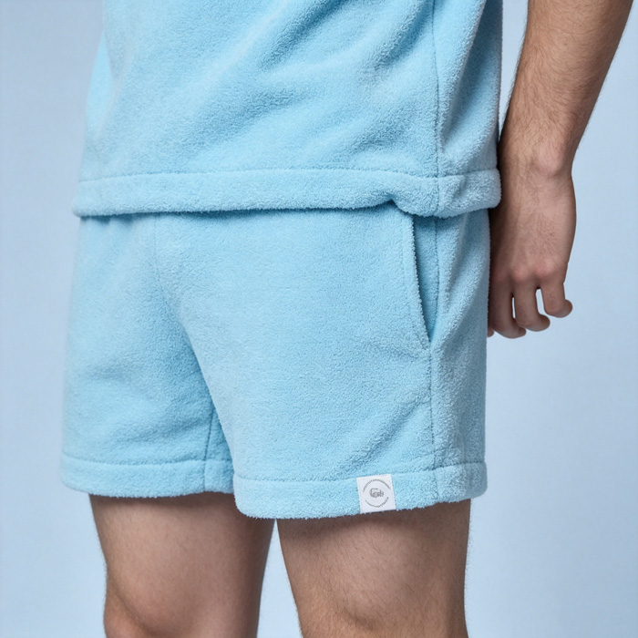 Male model angled back view wearing light blue Towel Shorts with side pocket and woven label, oem apparel manufacturer