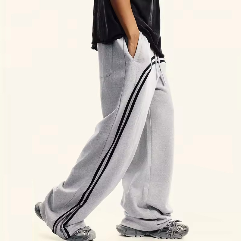 Side view of light gray baggy sweatpants with black curved stripes, showing wide leg silhouette and streetwear fit